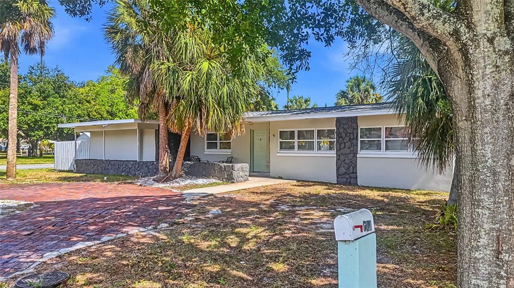 A single-story house with a brick driveway, palm trees, and a dark stone accent wall — 6400 PELICAN DRIVE S, ST PETERSBURG, FL
