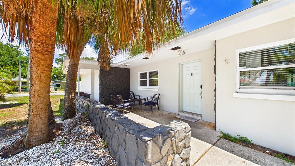 A light-colored house exterior features a stone wall, a covered porch, and a palm tree — 6400 PELICAN DRIVE S, ST PETERSBURG, FL