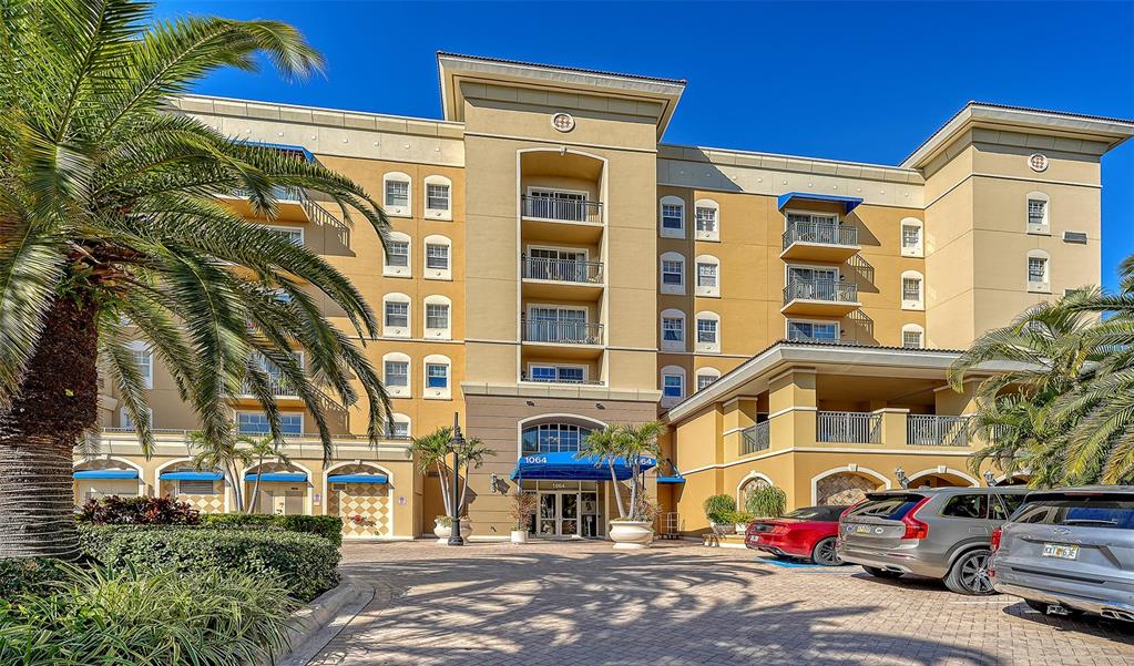 Exterior view of a multi-story tan apartment building with balconies and a paved driveway — 1064 N TAMIAMI TRAIL UNIT 1320, SARASOTA, FL