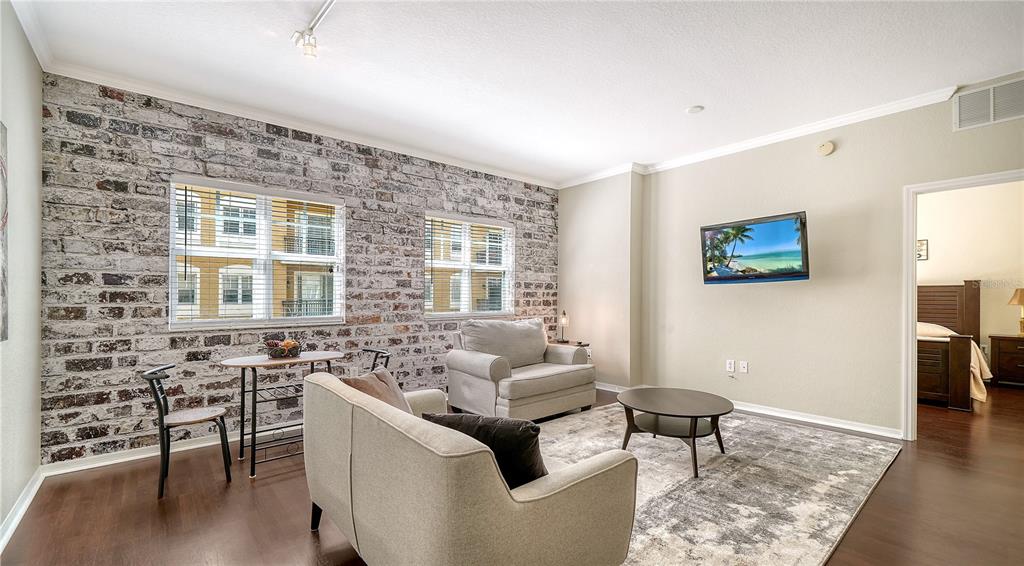 A living room features a rustic brick accent wall, hardwood floors, and neutral furniture — 1064 N TAMIAMI TRAIL UNIT 1320, SARASOTA, FL