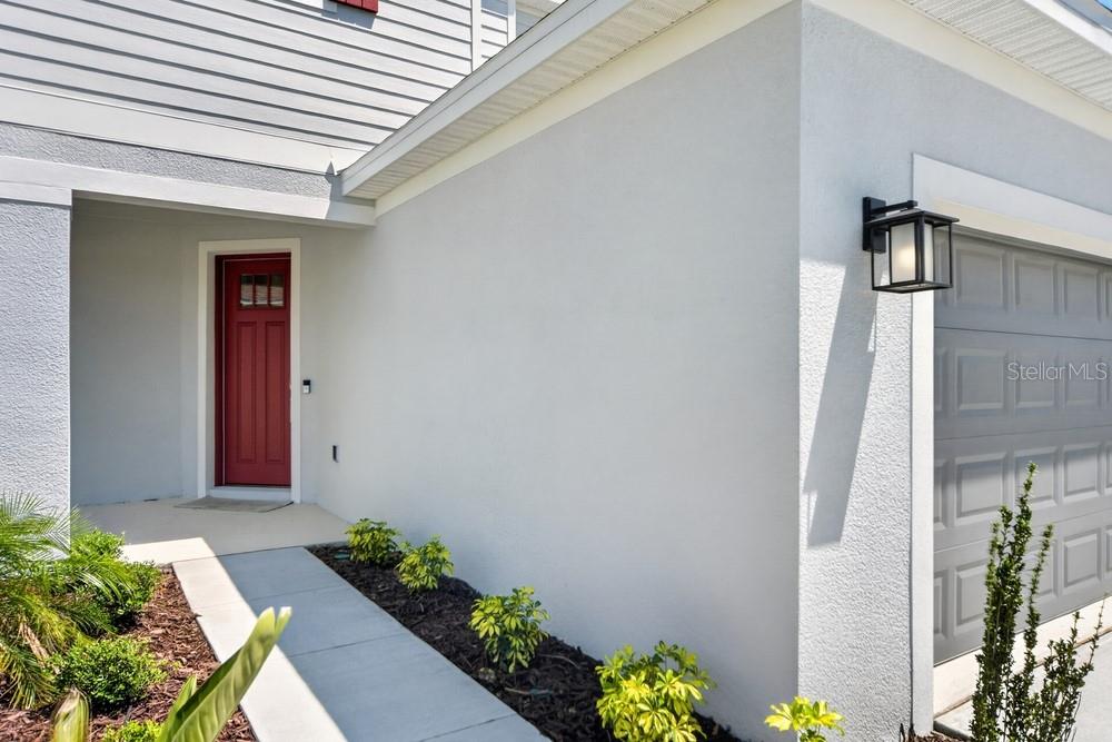A red front door is set back from a concrete walkway beside a gray garage — 5801 PORTICO PLACE, KISSIMMEE, FL