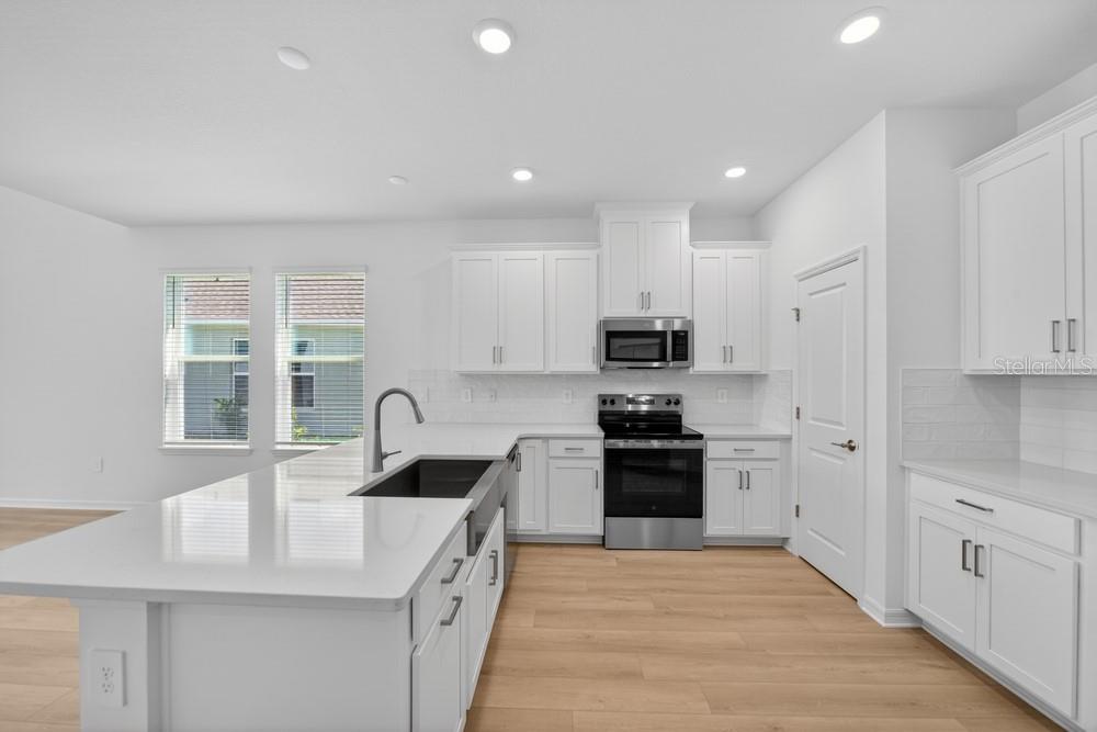 A modern kitchen features white cabinets, stainless steel appliances, a quartz island, and light wood flooring — 5801 PORTICO PLACE, KISSIMMEE, FL
