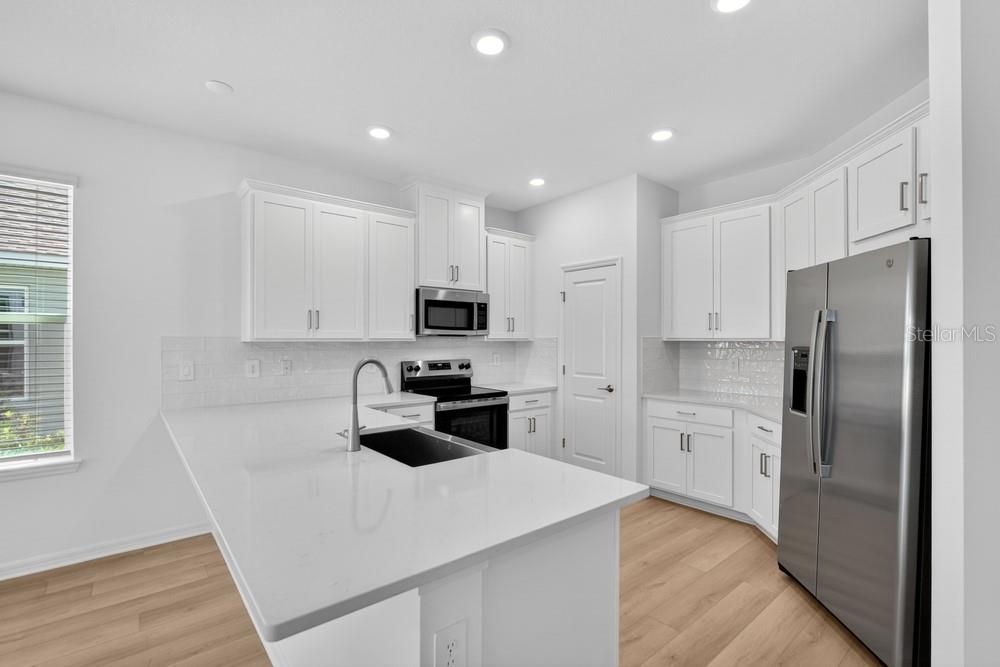 A modern kitchen features white cabinets, quartz countertops, stainless steel appliances, and light wood flooring — 5801 PORTICO PLACE, KISSIMMEE, FL