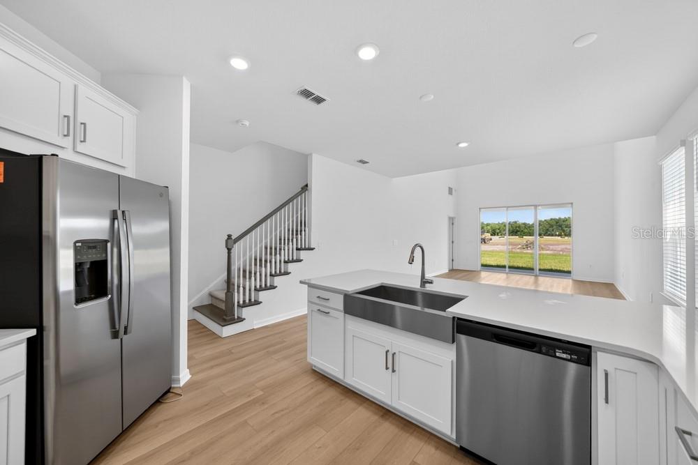 A modern kitchen features white cabinetry, stainless steel appliances, a farmhouse sink, and wood flooring — 5801 PORTICO PLACE, KISSIMMEE, FL