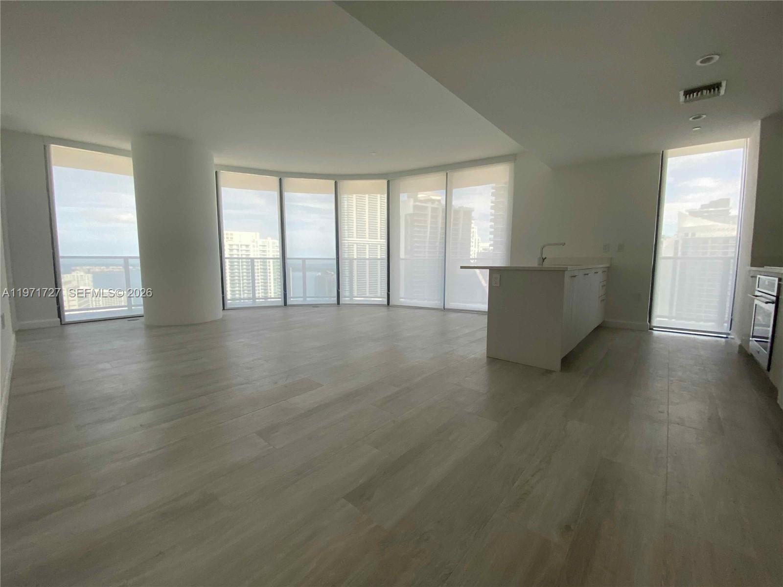 An open-concept living area features light wood-look flooring, a kitchen island, and floor-to-ceiling windows — 45 SW 9th St # 3703, Miami FL 33130, MIAMI, FL