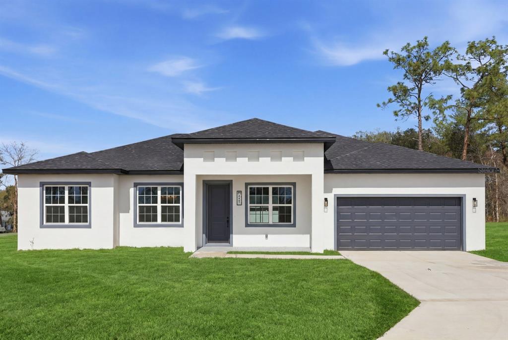 A single-story house with white stucco walls, a dark gray roof, and a two-car garage — 13715 SW 38TH COURT, OCALA, FL
