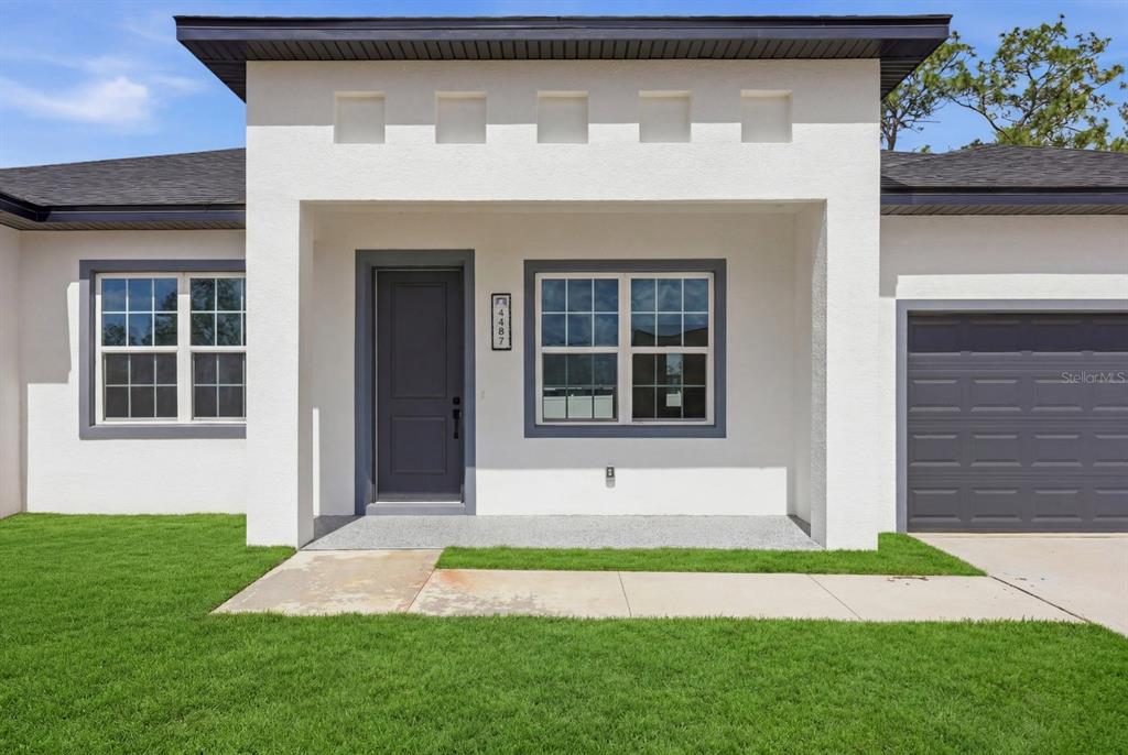 The exterior of a white house features a dark gray front door and garage door — 13715 SW 38TH COURT, OCALA, FL