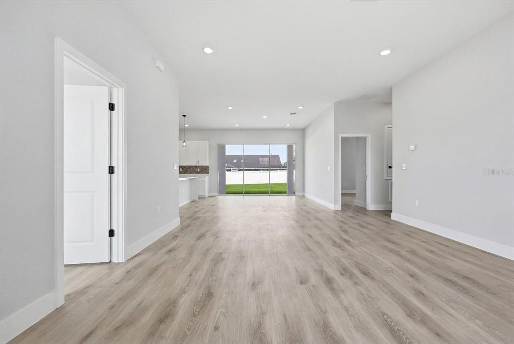 An open-concept living area features light wood-look flooring, white walls, and a sliding glass door — 13715 SW 38TH COURT, OCALA, FL