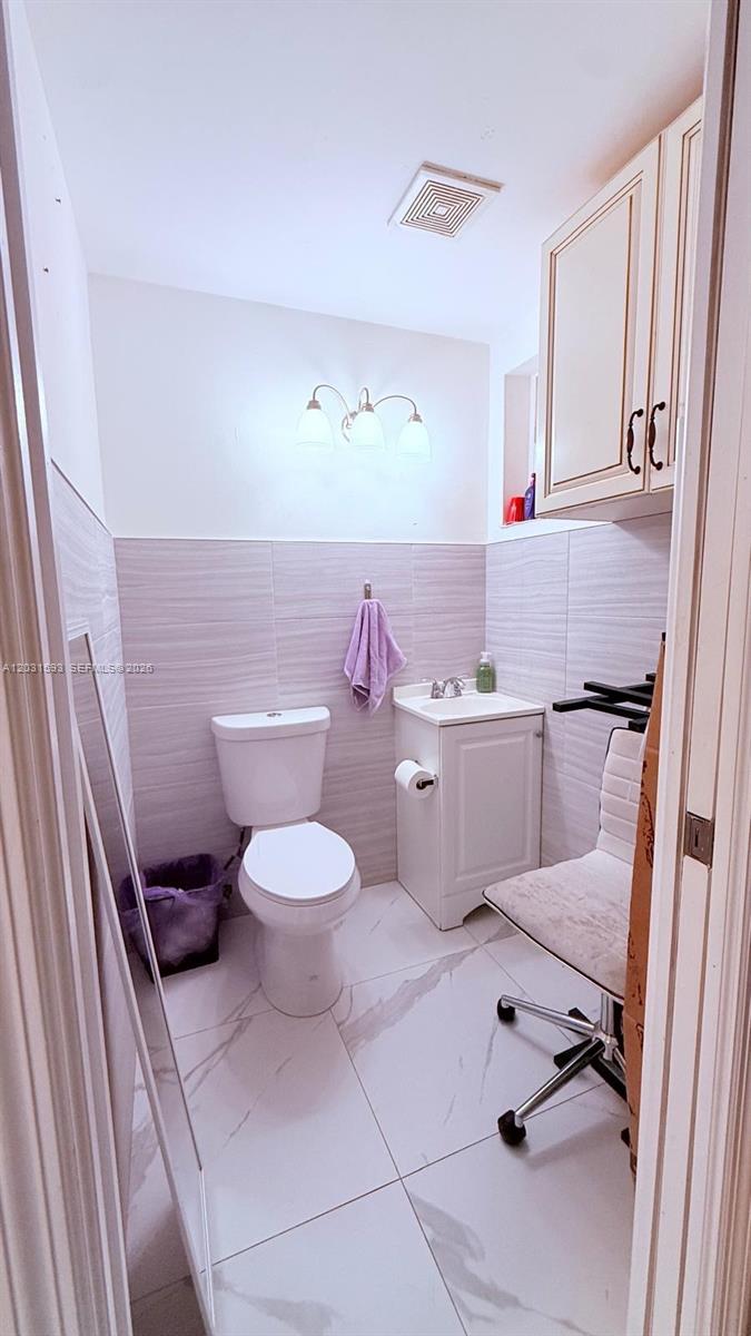 A small bathroom features a toilet, a pedestal sink, and light-colored tile walls and floors — Beauty Supply Store, Miami FL 33125, MIAMI, FL