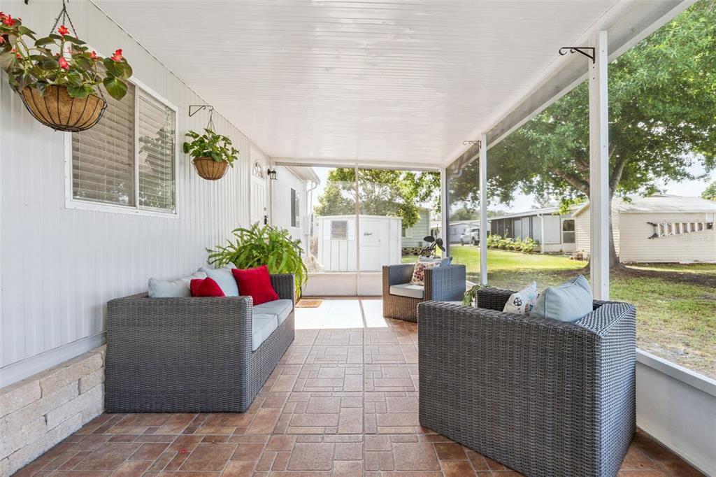 A screened-in porch features tiled flooring, wicker patio furniture, and hanging potted plants — 511 FLAMINGO LANE, OSTEEN, FL