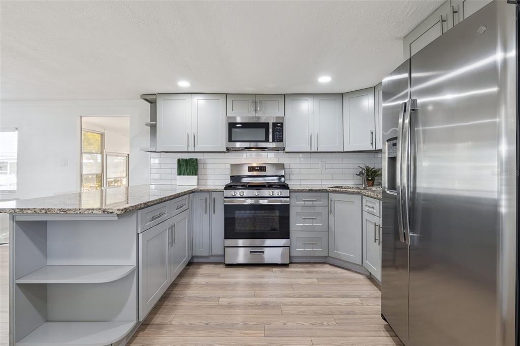 A kitchen features light gray cabinets, stainless steel appliances, granite countertops, and wood-look flooring — 511 FLAMINGO LANE, OSTEEN, FL