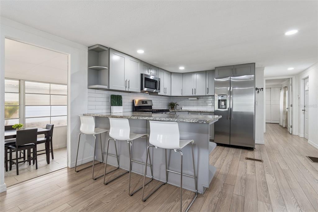 A modern kitchen features gray cabinets, granite countertops, stainless steel appliances, and three white barstools — 511 FLAMINGO LANE, OSTEEN, FL