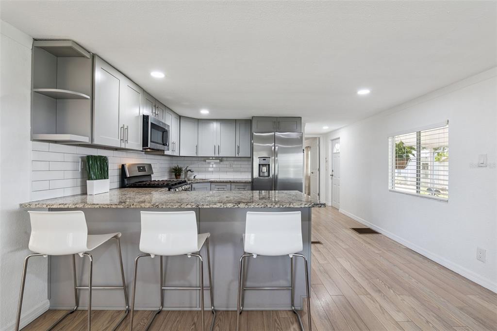 A kitchen features gray cabinets, granite countertops, a breakfast bar with stools, and wood flooring — 511 FLAMINGO LANE, OSTEEN, FL