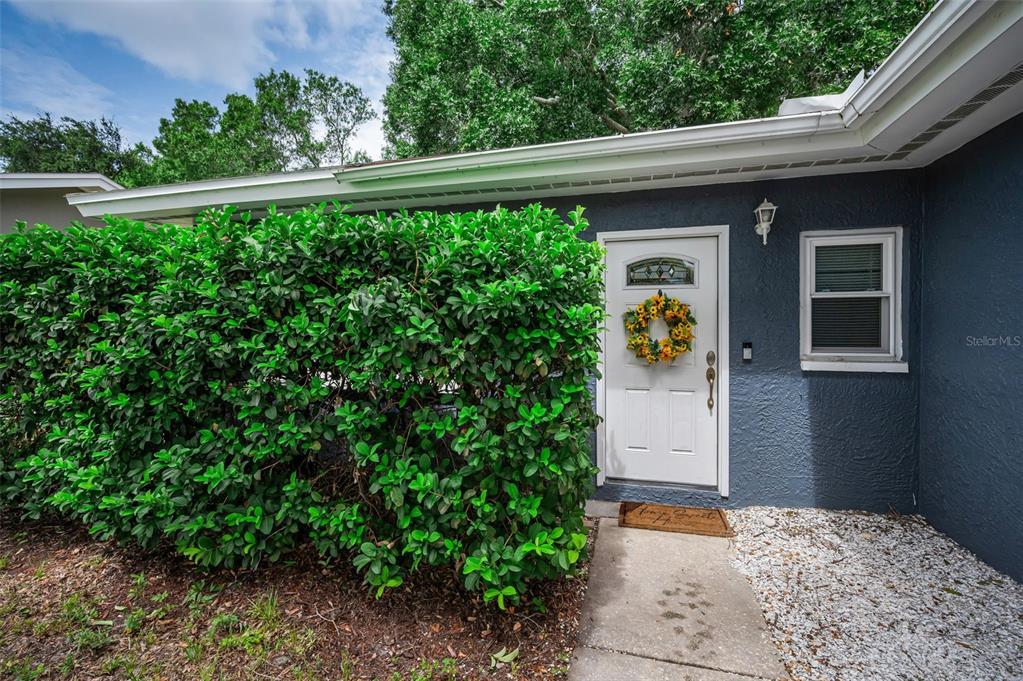 A white front door with a sunflower wreath sits beside a large green hedge — 1760 E ORANGESIDE ROAD, PALM HARBOR, FL