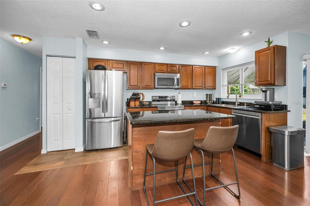 A kitchen features wood cabinets, stainless steel appliances, a granite island, and hardwood flooring — 1760 E ORANGESIDE ROAD, PALM HARBOR, FL