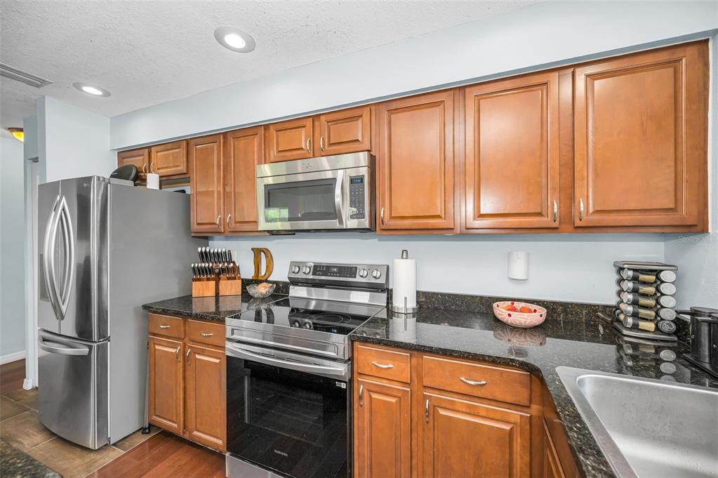 A kitchen features wood cabinets, stainless steel appliances, and dark granite countertops — 1760 E ORANGESIDE ROAD, PALM HARBOR, FL