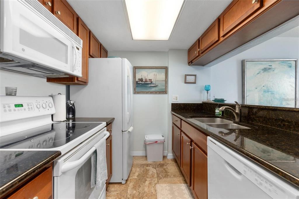 A galley kitchen features wood cabinets, dark granite countertops, white appliances, and tiled flooring — 3600 S OCEAN SHORE BOULEVARD UNIT 423, FLAGLER BEACH, FL