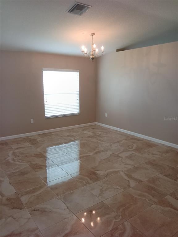 An empty dining room features beige walls, a chandelier, and polished light-brown tile flooring — 7724 OUTERBRIDGE STREET, WESLEY CHAPEL, FL