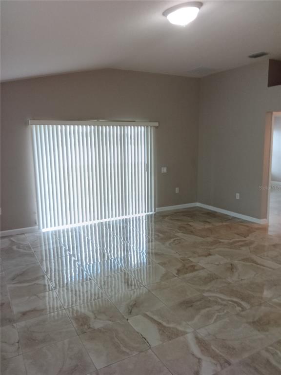 A room with light-colored tile flooring, a vaulted ceiling, and vertical blinds over sliding doors — 7724 OUTERBRIDGE STREET, WESLEY CHAPEL, FL