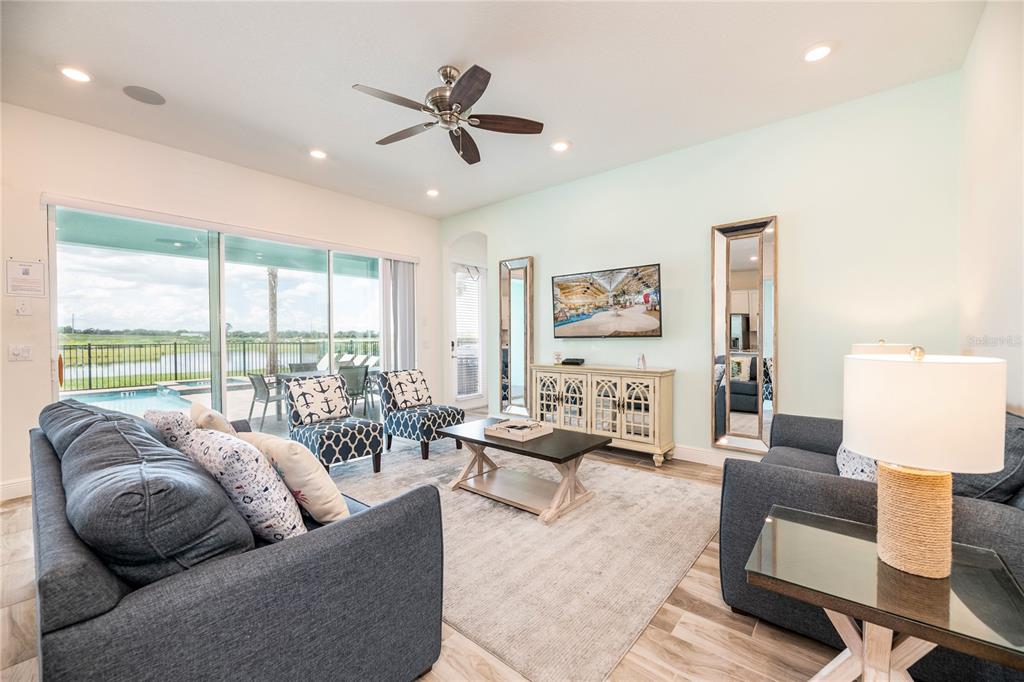 A living room features a blue sofa, patterned armchairs, a television, and a sliding glass door — 8145 SURF STREET, KISSIMMEE, FL
