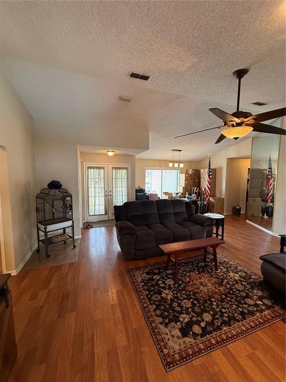 A living room features wood-look flooring, a dark sofa, a ceiling fan, and a birdcage — 9231 ELDRIDGE ROAD, SPRING HILL, FL