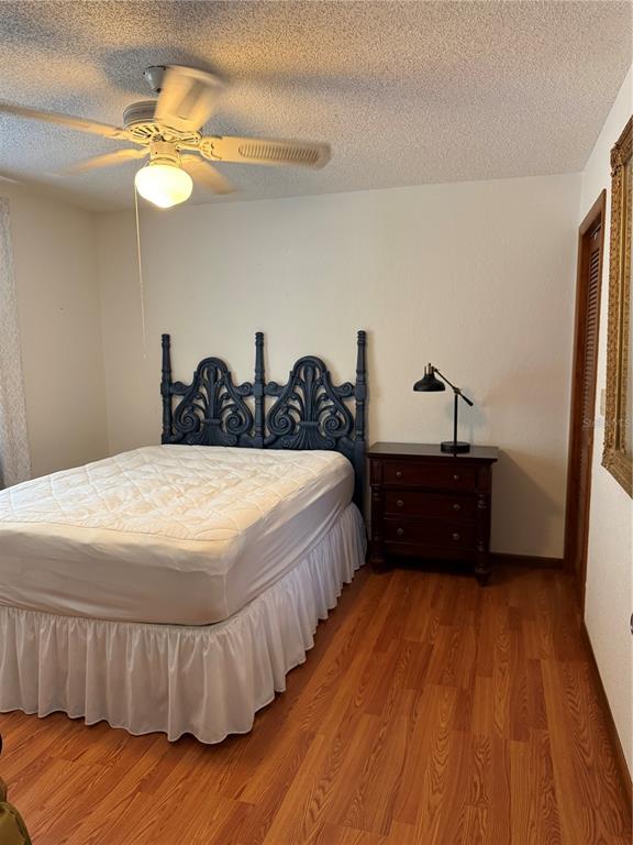 A bedroom features a dark blue ornate headboard, a white bed skirt, and wood flooring — 9231 ELDRIDGE ROAD, SPRING HILL, FL