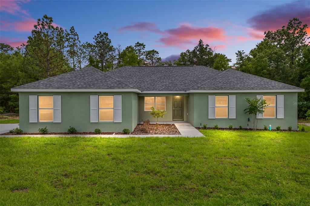 A single-story green house with a gray shingled roof and shutters at dusk — 3853 SW SOUNDVIEW DRIVE, DUNNELLON, FL