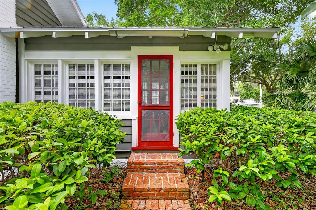 A red screen door leads to a brick-stepped porch with white-framed windows and green bushes — 1046 N MCDONALD STREET, MOUNT DORA, FL