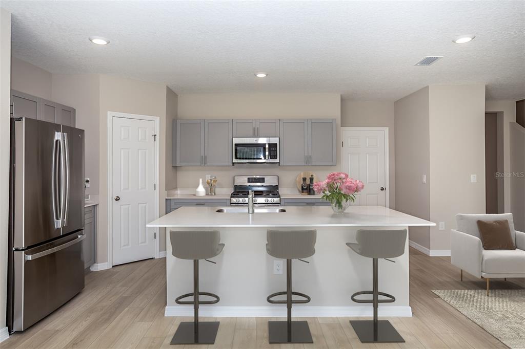 A modern kitchen features gray cabinets, stainless steel appliances, a white island, and bar stools — 5445 SAN PIETRO DRIVE, WINTER HAVEN, FL