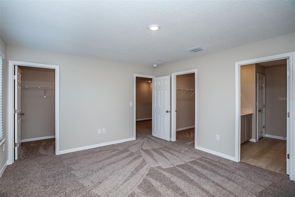 A bedroom with carpeted flooring, neutral walls, and three doorways leading to closets and a bathroom — 5445 SAN PIETRO DRIVE, WINTER HAVEN, FL