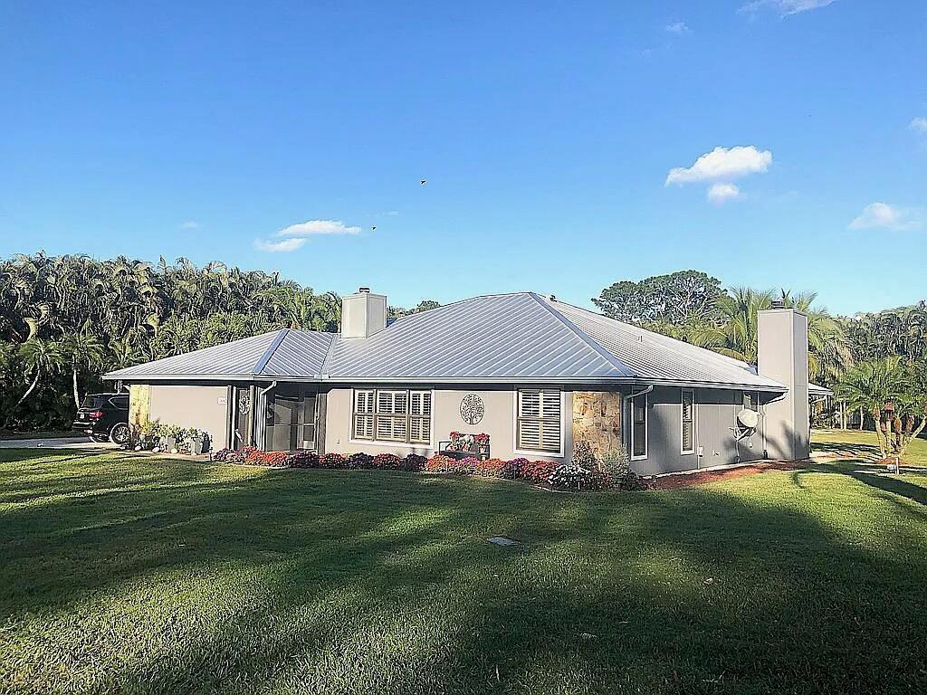 A single-story house with a metal roof, gray siding, and two chimneys sits on grass — 16826 126th Terrace N, Jupiter FL 33478, JUPITER, FL