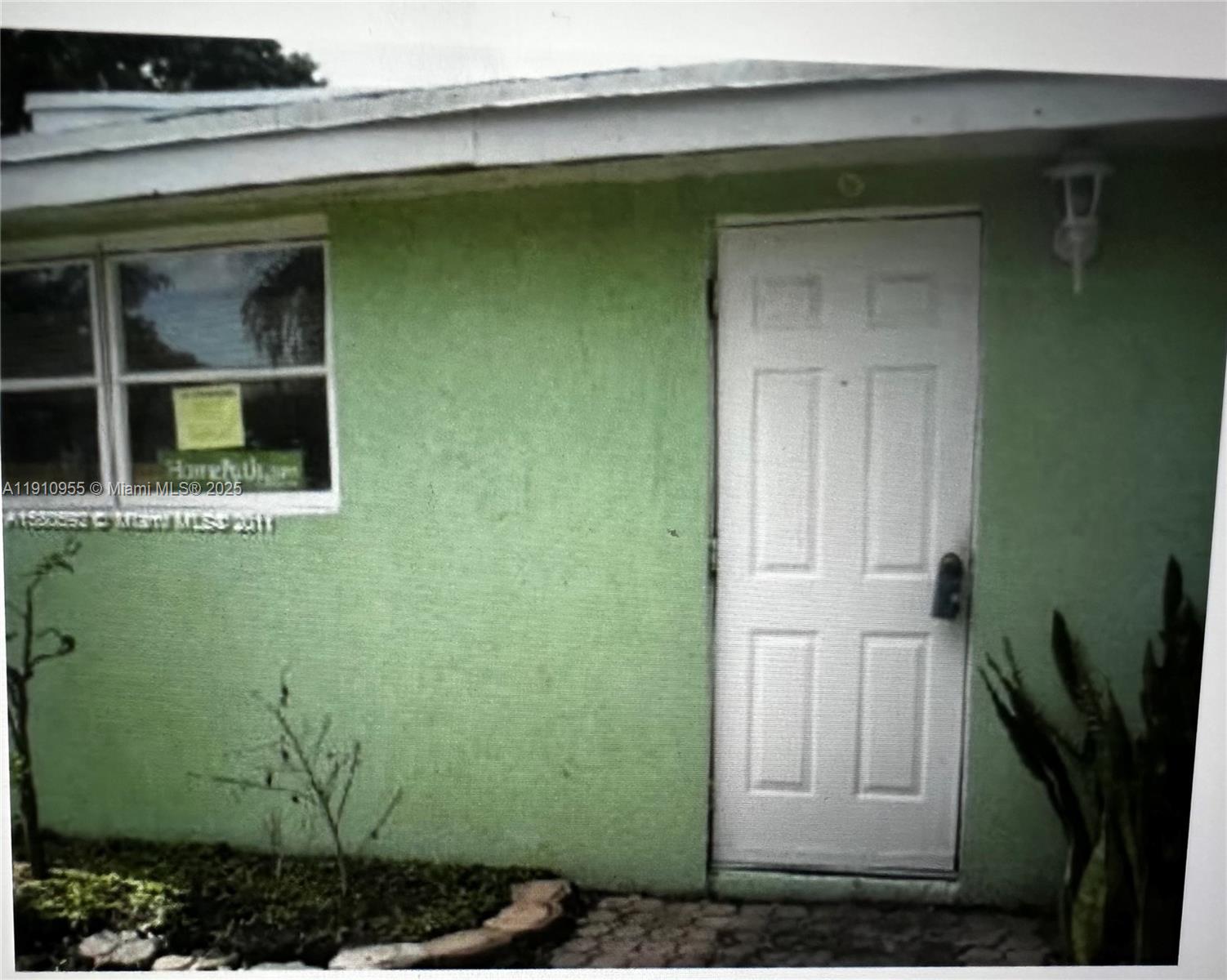 A green exterior wall features a white door, a window with a sign, and landscaping — 3490 SW 56th Ave, West Park FL 33023, WEST PARK, FL