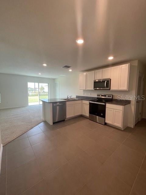 A kitchen with white cabinets, granite countertops, and stainless steel appliances overlooks an open living area — 10231 OPALINE SKY COURT, RIVERVIEW, FL