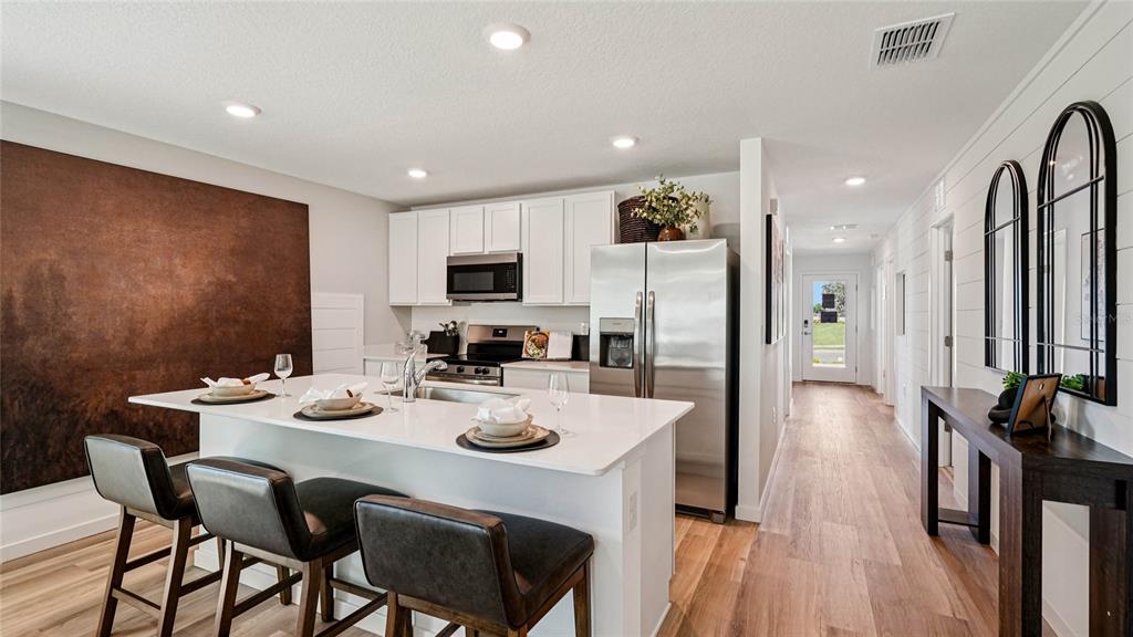 A kitchen features white cabinets, a central island with bar seating, and stainless steel appliances — 7828 SW 46TH COURT, OCALA, FL