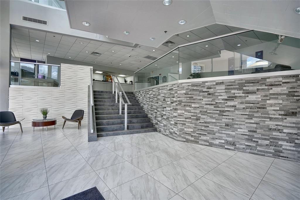 A modern lobby features a staircase, textured accent walls, and large light-colored floor tiles — 151 E WASHINGTON STREET UNIT 525, ORLANDO, FL
