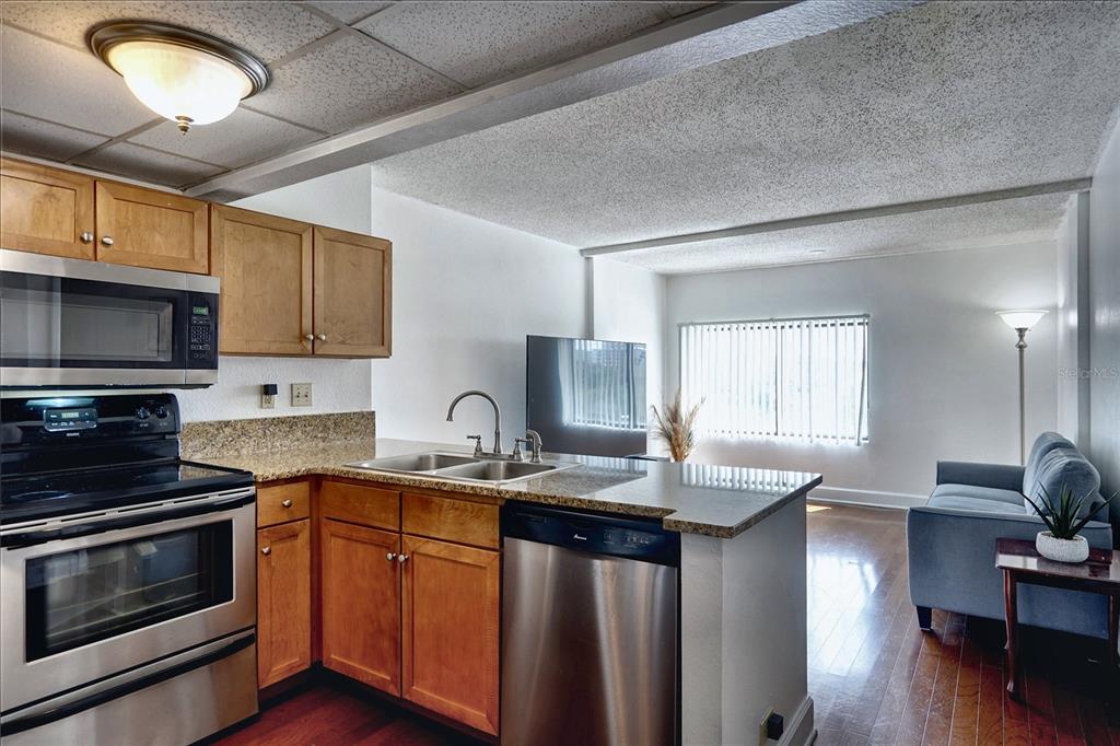 A kitchen with wood cabinets and stainless steel appliances opens into a living room area — 151 E WASHINGTON STREET UNIT 525, ORLANDO, FL
