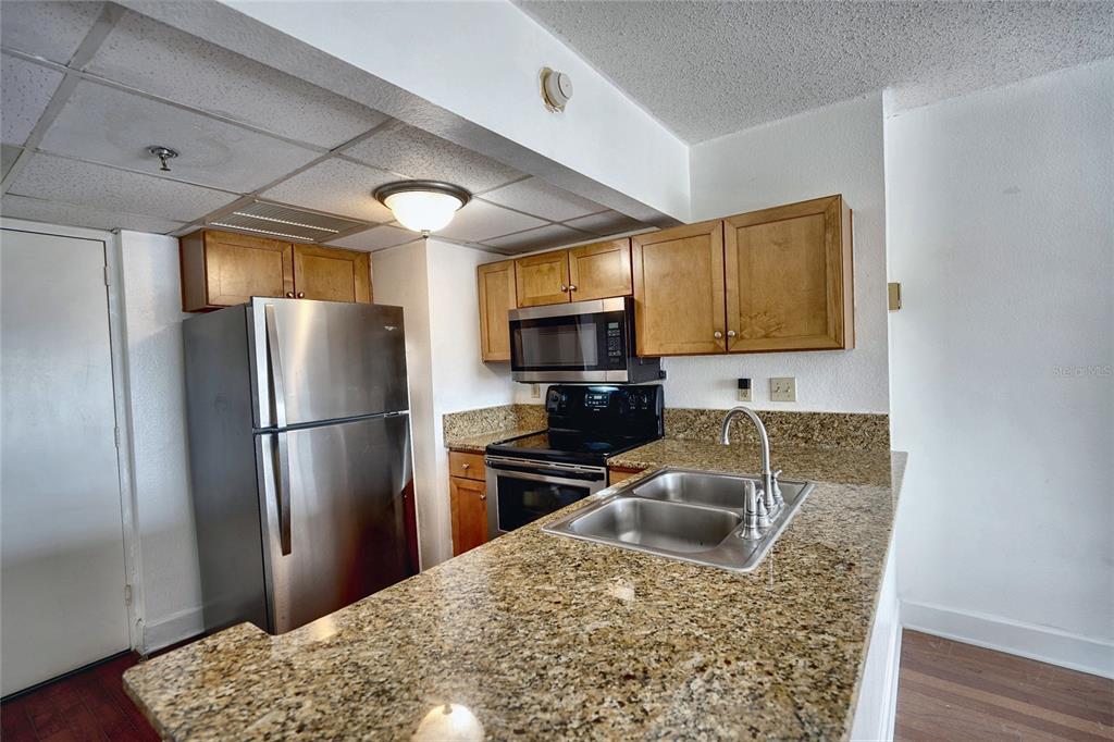 A kitchen features stainless steel appliances, wood cabinets, and granite countertops with a double sink — 151 E WASHINGTON STREET UNIT 525, ORLANDO, FL