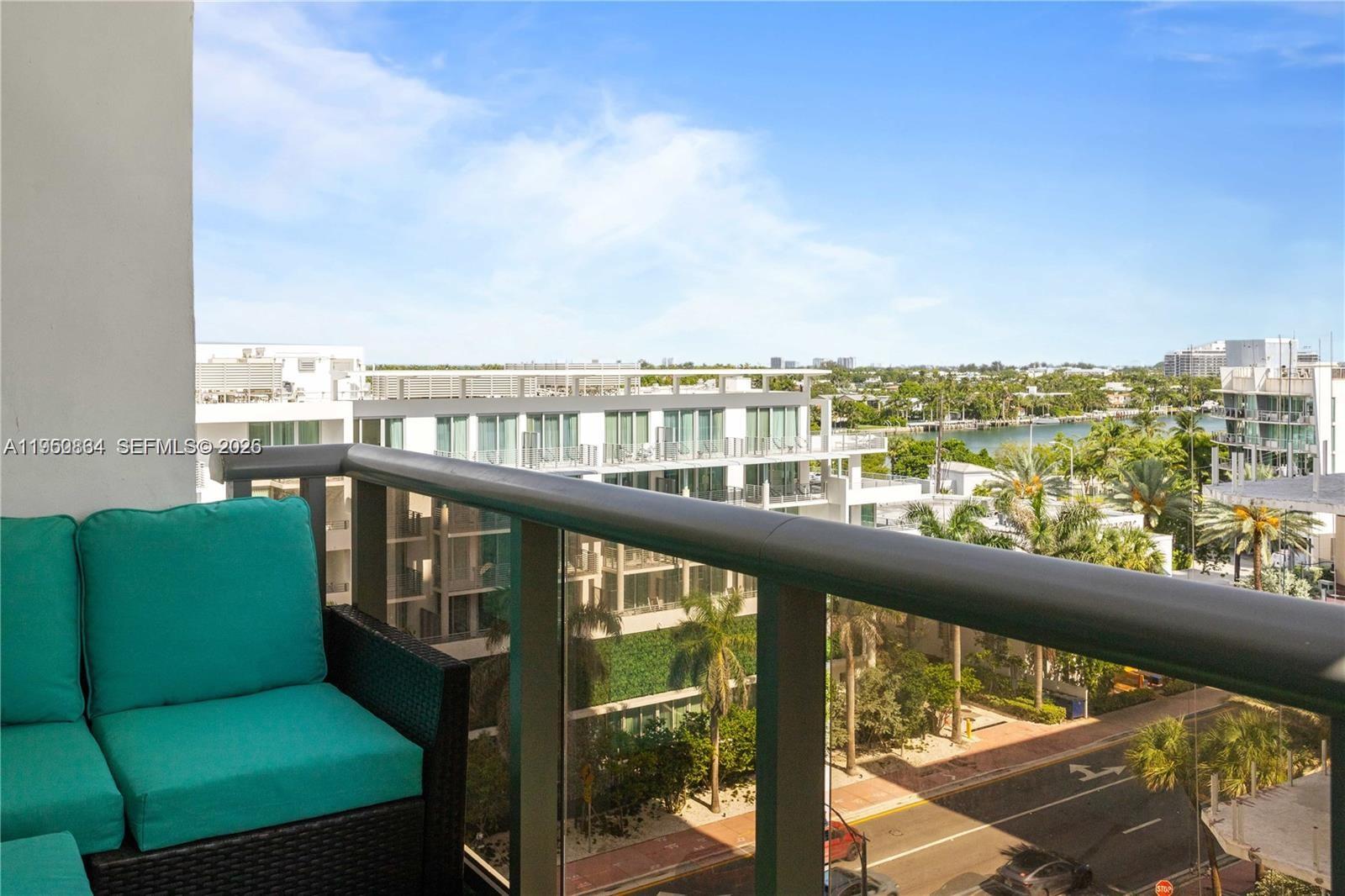 A balcony with teal cushions overlooks a street, palm trees, and a nearby waterway — 6039 Collins Ave # 809, Miami Beach FL 33140, MIAMI BEACH, FL