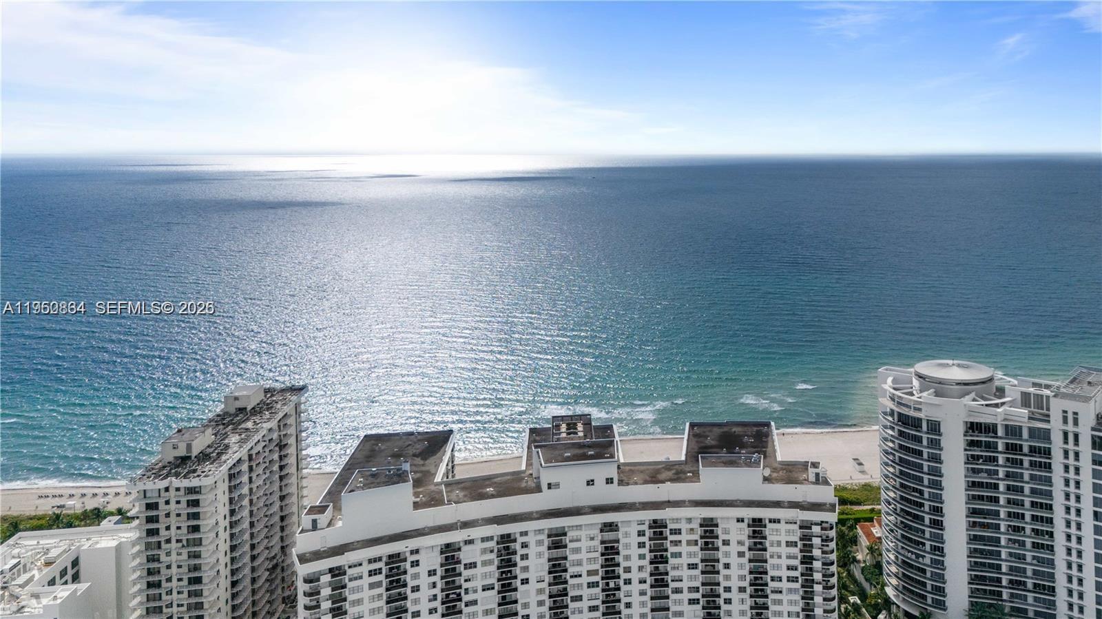 An aerial view shows high-rise residential buildings situated along a sandy beach and ocean — 6039 Collins Ave # 809, Miami Beach FL 33140, MIAMI BEACH, FL