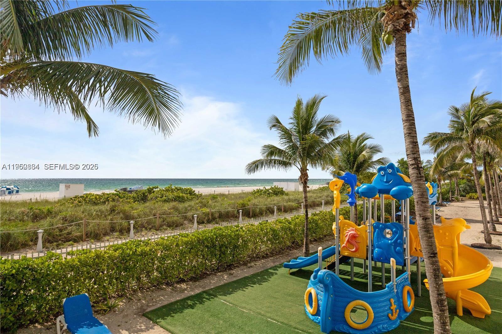 A playground with a blue boat-shaped structure sits on a lawn overlooking the beach — 6039 Collins Ave # 809, Miami Beach FL 33140, MIAMI BEACH, FL