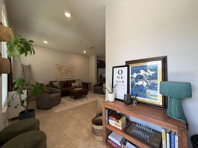 A living room with tile flooring features a brown sofa, an armchair, and a wooden bookshelf — 5030 CASPIAN STREET, ST CLOUD, FL