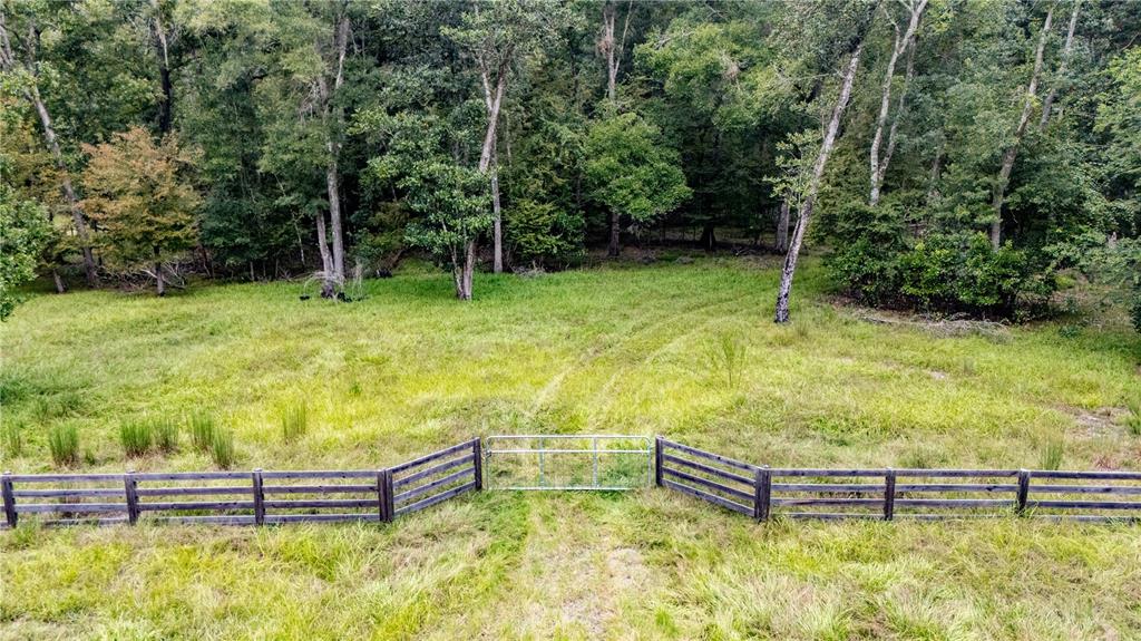 A metal gate connects two sections of a wooden fence in a grassy, wooded field — 26840 NW 206TH PLACE, HIGH SPRINGS, FL