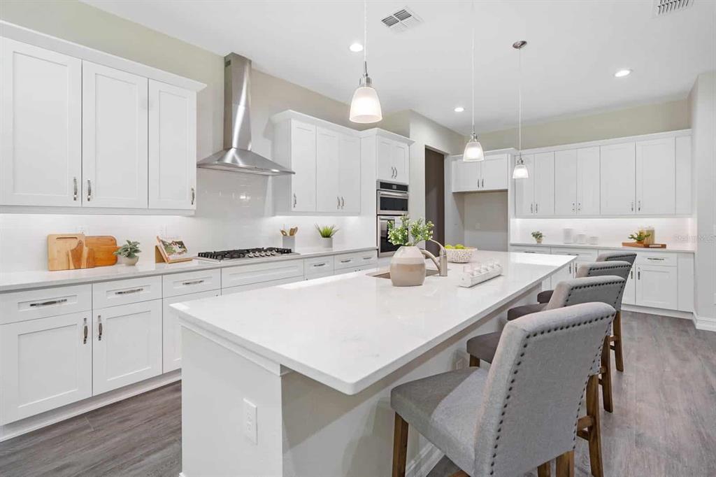 A modern white kitchen features a large quartz island, stainless steel appliances, and gray flooring — 4766 MAJESTIC HILLS LOOP, BROOKSVILLE, FL