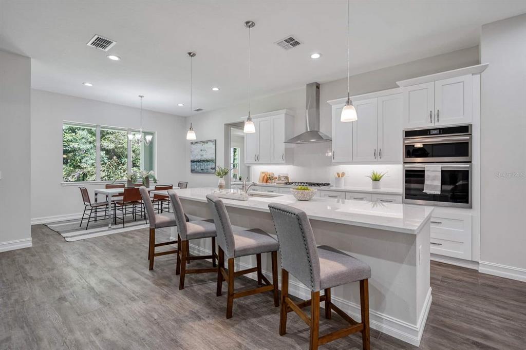 A modern kitchen features white cabinetry, a large island with bar stools, and an adjacent dining area — 4766 MAJESTIC HILLS LOOP, BROOKSVILLE, FL