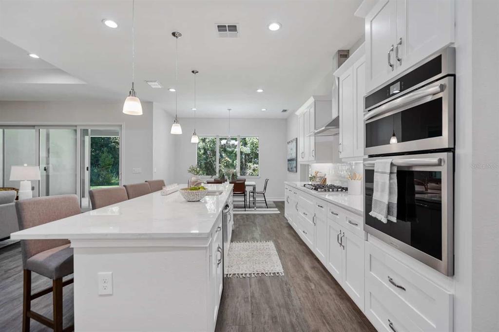 A modern white kitchen features a large marble-topped island, stainless steel appliances, and wood flooring — 4766 MAJESTIC HILLS LOOP, BROOKSVILLE, FL