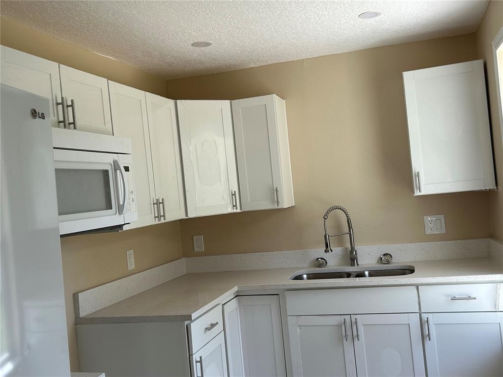 A kitchen features white cabinets, a microwave, a double sink, and light-colored countertops — 400 S 6TH STREET, LEESBURG, FL