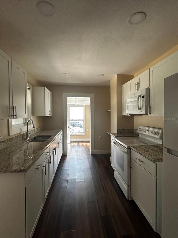 A galley kitchen features white cabinets, granite countertops, stainless steel appliances, and dark wood flooring — 400 S 6TH STREET, LEESBURG, FL