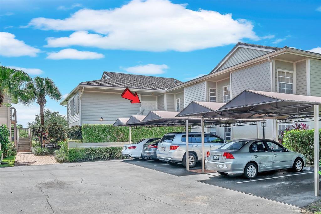 A multi-story apartment building exterior features a covered parking area and a red arrow pointing to an upper-level entrance — 7644 Elmridge Drive, Boca Raton FL 33433, BOCA RATON, FL