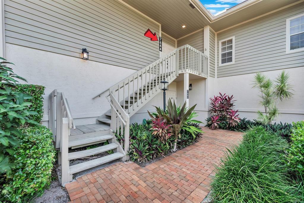 An exterior view of a two-story building with a wooden staircase leading to an upper entrance — 7644 Elmridge Drive, Boca Raton FL 33433, BOCA RATON, FL