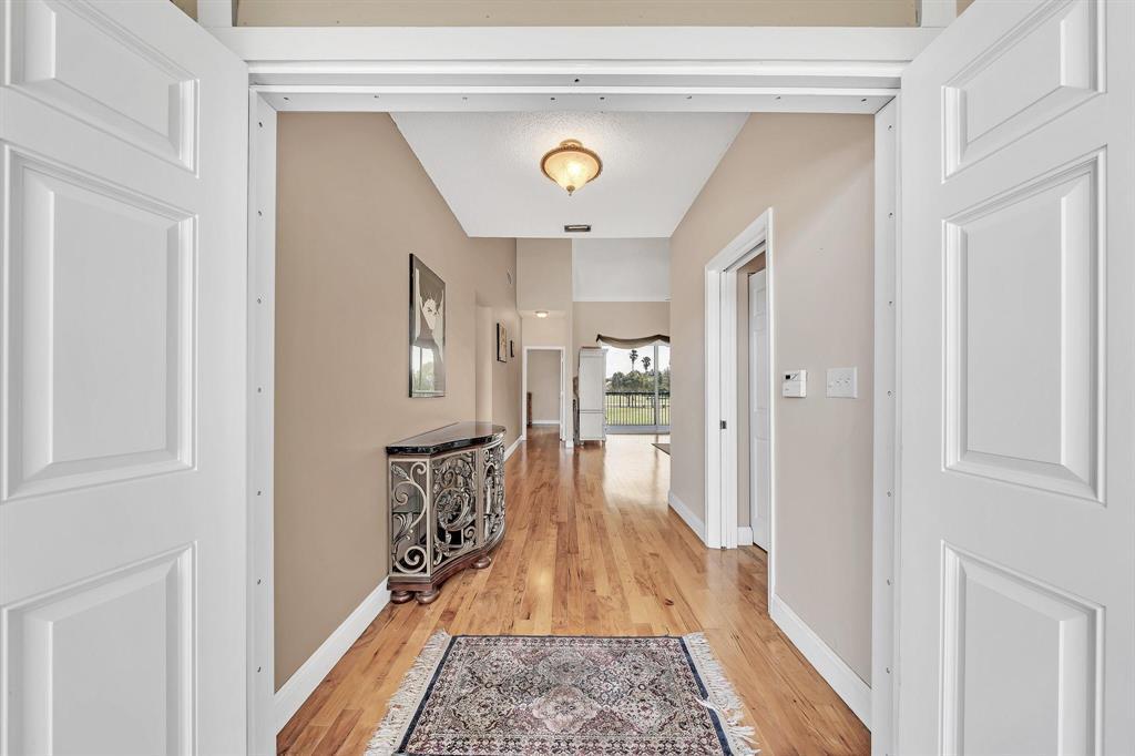 A hallway with hardwood floors and a decorative console table leads toward a distant window — 7644 Elmridge Drive, Boca Raton FL 33433, BOCA RATON, FL